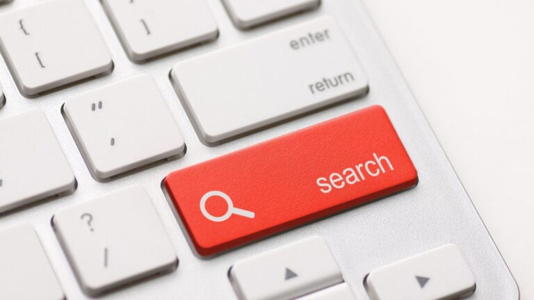 Close-up of a computer keyboard with a prominent red key labeled "search" featuring a magnifying glass icon, replacing the usual key in the position next to the "enter" key.