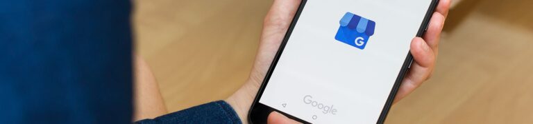 A person holding a smartphone displaying the Google My Business app logo on the screen.