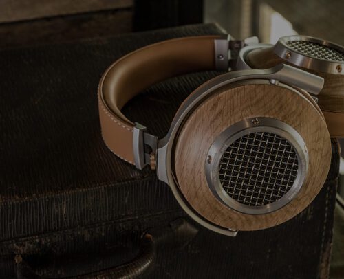 A pair of over-ear headphones with wooden ear cups and metal mesh rests on a textured, dark suitcase.