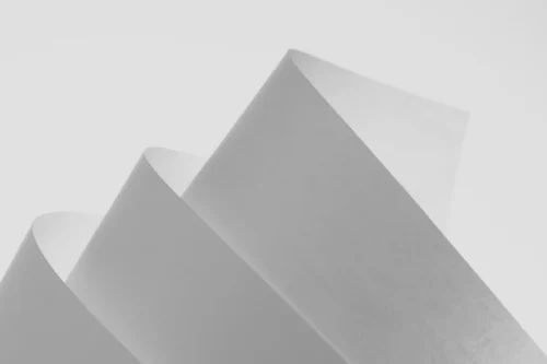 Three white sheets of paper are layered and folded in a minimalist, abstract arrangement against a plain light background.